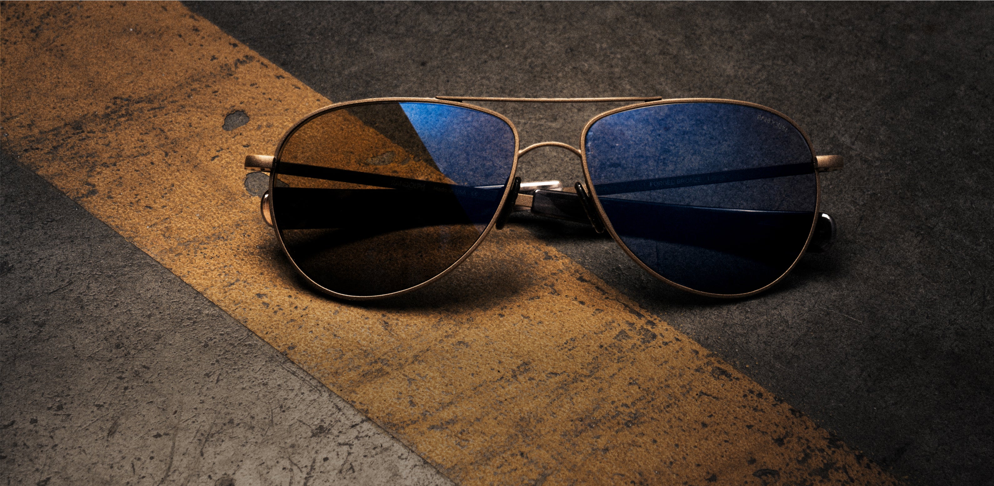 RANDOLPH Hawk sunglasses from the Shelby collection with Daytona blue lenses on a worn racing surface.